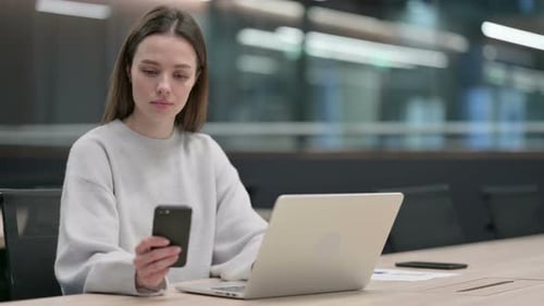 Young Woman Uses Laptop and Phone in Modern Office