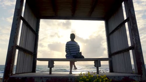 Woman Sits on Beach Bench at Sunset