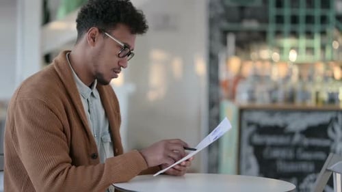 African Man Writing on Paper in Cafe