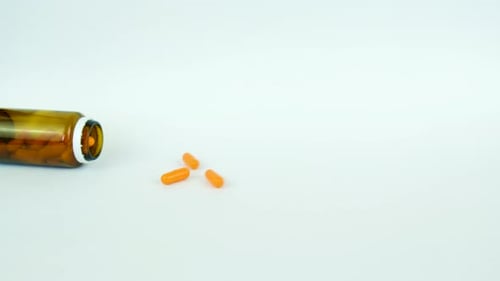 Orange Capsules Pouring from Amber Bottle