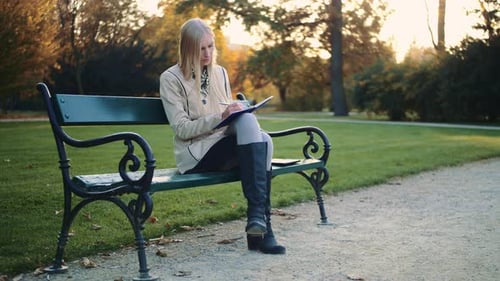 Young Woman Is Writing a Diary Outdoors in the Park