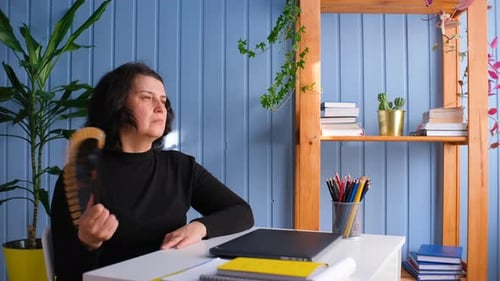 Woman Fanning Herself at Desk in Home