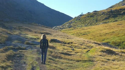 Slow motion: woman with backpack hiking in high altitude mountain environment, dramatic alpine lands