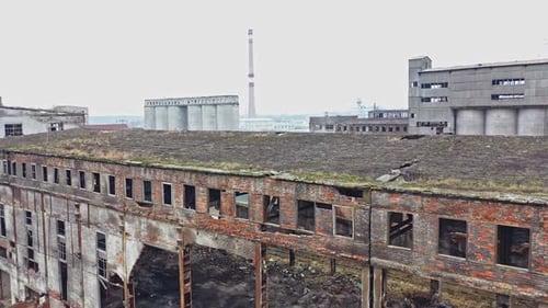 An old abandoned factory hangar with damaged walls on the background of other old structures