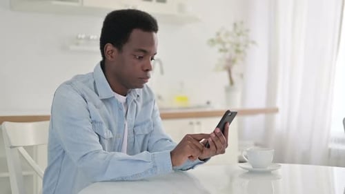 Man Sitting at Table Using Smartphone, Celebrates