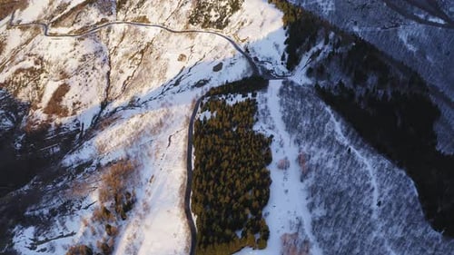 Vue aérienne panoramique de la forêt enneigée et de l'autoroute incurvée pendant le coucher du soleil.Route à travers la montagne