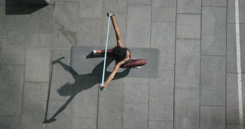Black Woman Does Dynamic Lunges with Elastic Band on Street