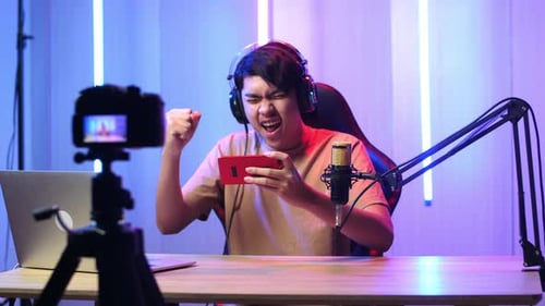 Asian Man Playing Video Game With Mobile Phone Then Celebrating While Live Stream With Camera