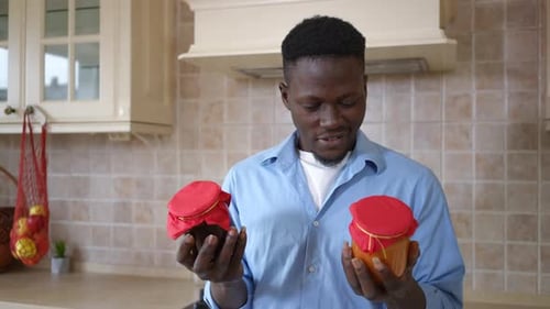 Portrait d'un homme afro-américain satisfait étirant des pots avec de la confiture souriant en regardant la caméra
