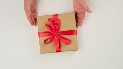 two female hands put on a white table a wrapped square box