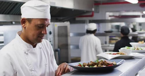 Caucasian male chef garnishing dish and smiling in restaurant kitchen
