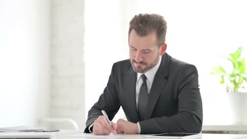 Young Businessman Writing on Paper in Office
