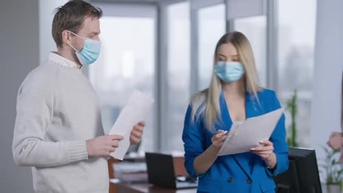 Coworkers Review Documents in Modern Office Wearing Masks