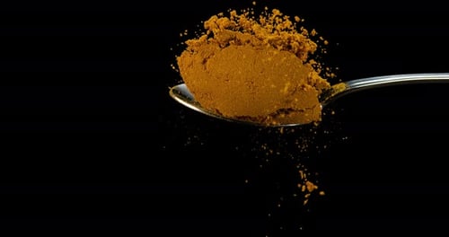 Spoon and Curry Powder falling against Black Background, Slow motion 4K