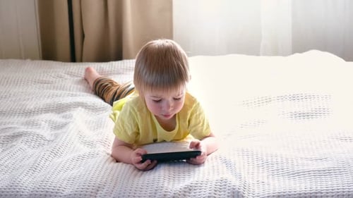 Child Relaxing with Smartphone on Bed at Home