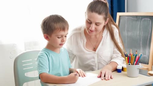 Boy Drawing at Table with Smiling Woman