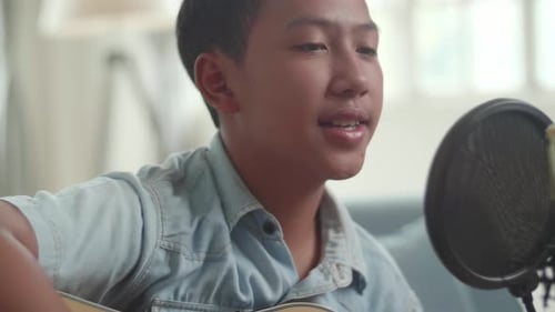 Chico asiático tocando la guitarra y cantando una canción
