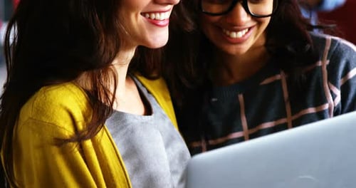 Smiling Women Collaborate Over Laptop in Workplace