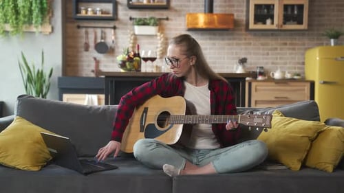 Woman Playing Guitar on Sofa at Home