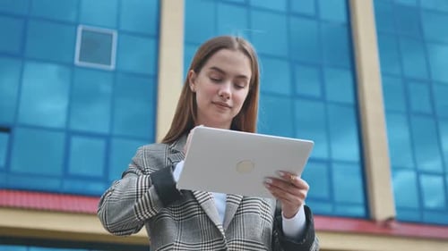 A Young Girl Student Works with a White Tablet in the City