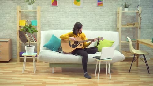 Woman Plays Guitar at Home with Laptop