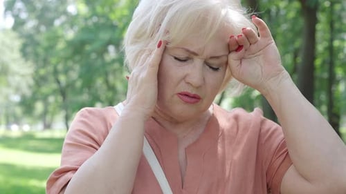 Portrait rapproché d'une belle femme âgée souffrant de maux de tête et de migraine dans un parc d'été ensoleillé