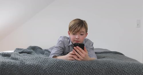 Boy Using Phone Lying on Bed at Home