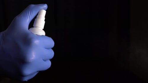 Gloved Hand Spraying Disinfectant Against Black Background