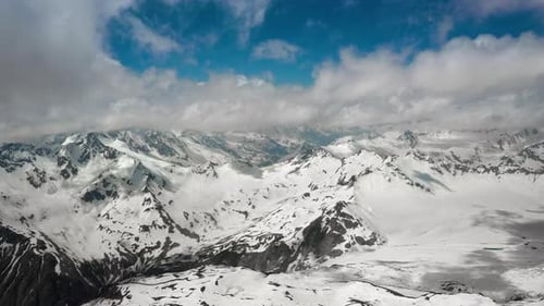 Air Flight Through Mountain Clouds Over Beautiful Snowcapped Peaks of Mountains and Glaciers