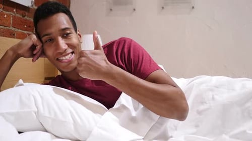 Pouces levés par un homme africain heureux allongé dans son lit sur le côté