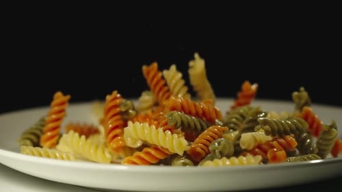 Colorful Rotini Pasta Falling onto White Plate
