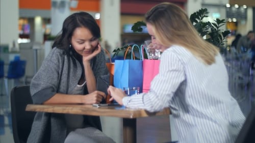 Two women using smartphones at cafe in shopping mall