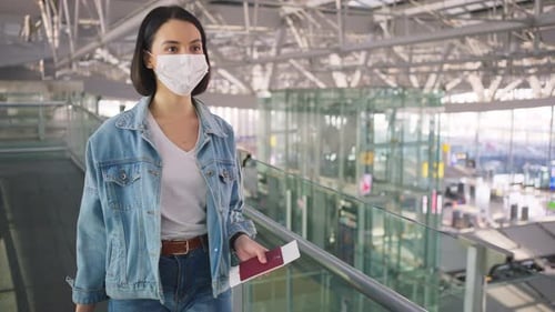 Asian woman passenger wearing face mask, walking in airport terminal to boarding gate to airplane.