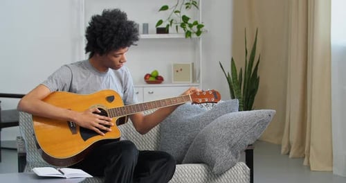 Young Adult Tuning Acoustic Guitar on Sofa