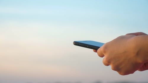 Woman's Hand Using Mobile Phone with A Clear Sky in The Background