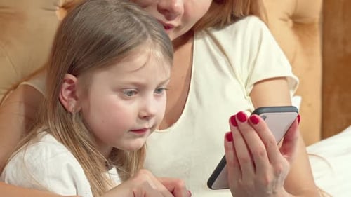 Woman and Child Using Smartphone Together in Bed