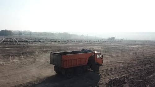 Construction Vehicle Dump Truck Loaded with Dirt is Driving in the Dust