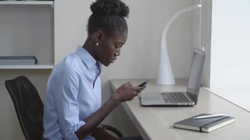 Woman Using Cellphone at Desk with Laptop