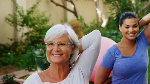 Senior woman with female trainer doing stretching exercise in garden 4k
