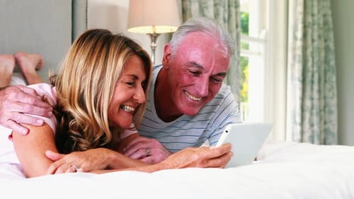 Senior Couple Laughing Together Using Tablet in Bedroom