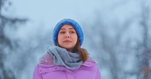 Beautiful Young Woman Walks in a Snowcovered Hat and Jacket Snow is Falling
