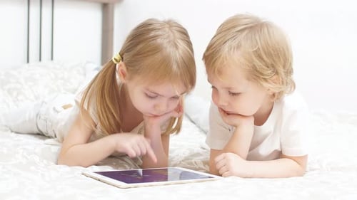 Little Caucasian Kids Use Tablet Sitting on Bed