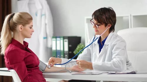 Smiling Female Medical Worker Measuring Pressure to Girl Patient at White Room Clinic Interior