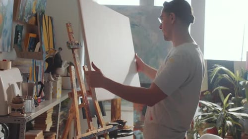 Man Placing Canvas on Easel in Art Studio