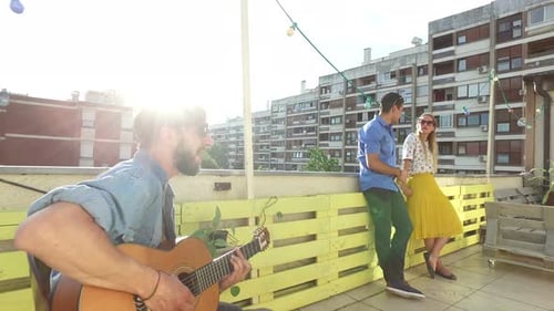 Man Plays Guitar for Friends on City Rooftop