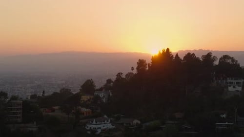 Aerial of houses on mountain top overlooking cityscape at sunset