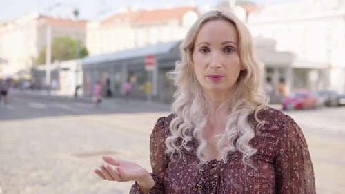 A Middleaged Caucasian Woman Talks to the Camera in an Urban Area