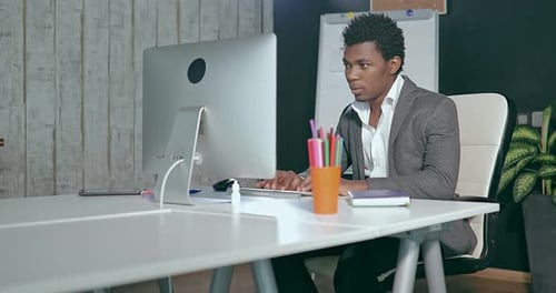 African Businessman in the Office in Front of the Computer Screen and Typing on Keyboard