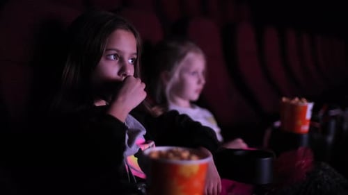 Caucasian Girl Watching a Movie or Cartoon in the Cinema with Her Sister in the Background
