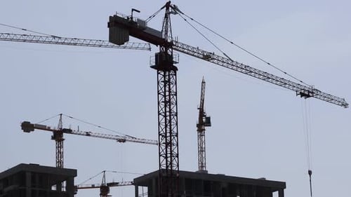 Construction Cranes At Work Against Blue Sky